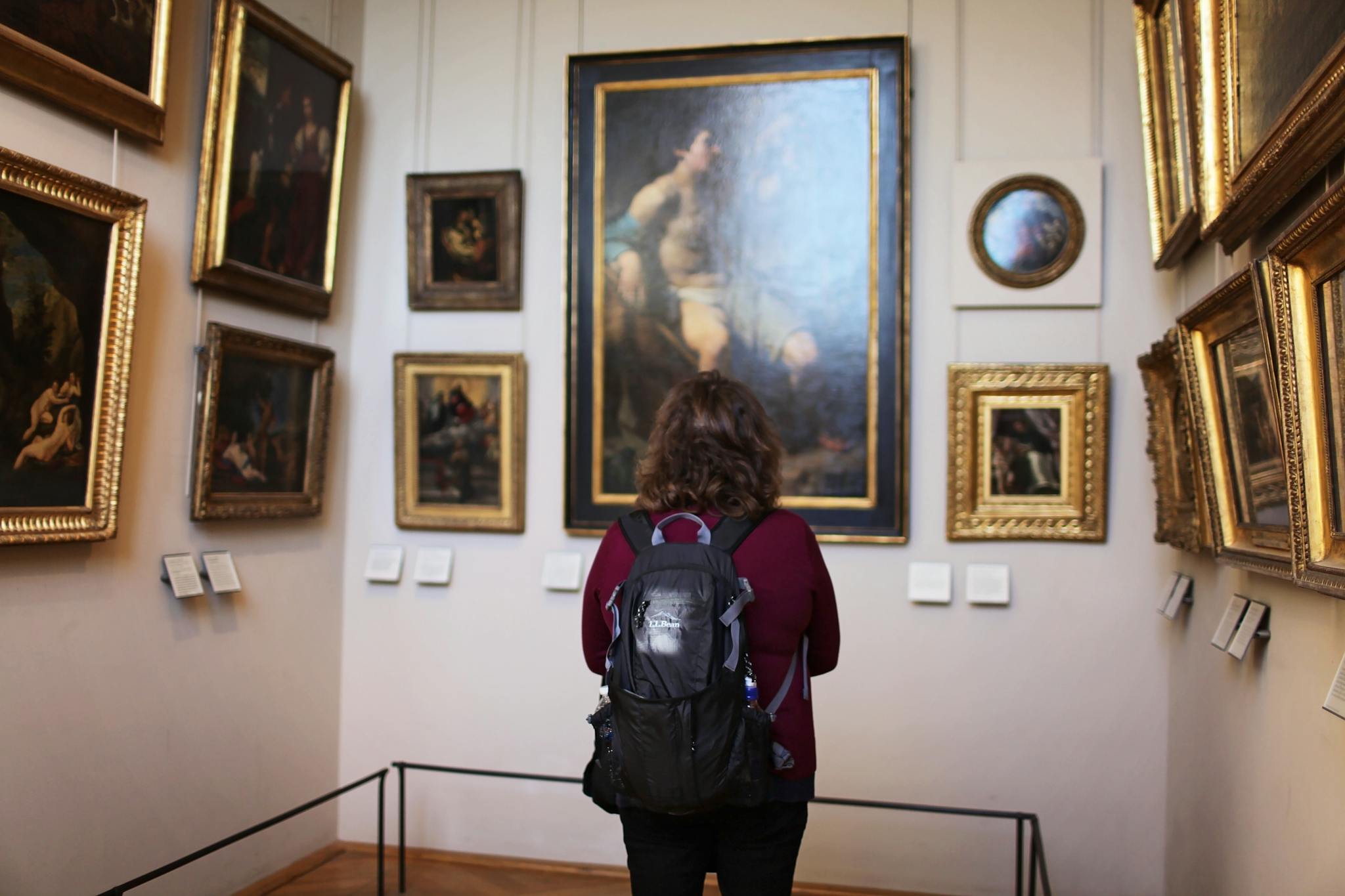 A visitor observes classic paintings in a tranquil museum gallery setting.